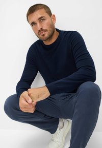 Dunkelblauer Strickpullover mit Rundhalsausschnitt, kombiniert mit blauen Hosen und weißen Sneakers. Minimalistisches Design mit glatter Textur.