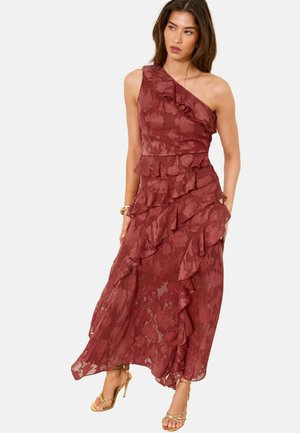 Vrouw draagt een mouwloze, een schouder roest-rode bloemen kanten jurk met gelaagde ruches en gouden hoge hakken sandalen.