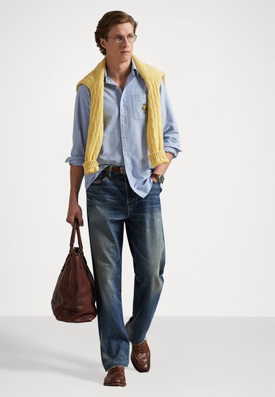 Gaiši zilā pogas kreklā, dzeltenā adītā džemperī, zilos džinsos, brūnās ādas kurpēs un brūnā ādas somā. Vienkāršs un ikdienišķs dizains.