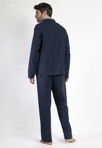 Conjunto de pijama de algodón a rayas navy con una camiseta de mangas largas y pantalones holgados, que presenta rayas verticales blancas y un cuello abotonado.