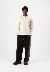 Lys beige genser med ribbestrikkede mansjetter, parret med løstsittende svarte joggebukser. Teksturert svart strikket lue og svarte/røde sneakers fullfører antrekket.