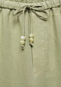 Jasnozielone lniane szorty z elastycznym pasem i dwoma dekoracyjnymi koralikami, subtelną teksturą oraz boczną kieszenią.