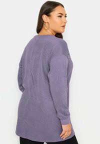 Lila långärmad tunika med ribbad textur och rundad nederkant. Har sidodetaljer och rund halsringning.