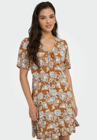 Bruine bloemenjurk met korte mouwen, V-hals, strikdetail en gerimpelde zoom; heeft blauwe en crèmekleurige bloemenpatronen op een gestructureerde stof.