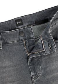 Jeans de mezclilla gris oscuro con cremallera metálica, cierre de botón y etiqueta interna. Cuenta con un diseño de cinco bolsillos y detalles de costura sutiles.
