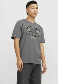 Grijze katoenen T-shirt met een ronde halslijn, korte mouwen en een zwart-geel grafisch ontwerp met merktekst en oprichtingsjaar.