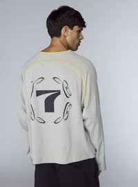Felpa grigia chiaro con maniche lunghe, presenta un grande numero 7 nero sul retro, evidenziato da cuciture gialle lungo le cuciture.