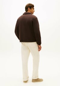 Brązowa polarowa kurtka z kołnierzem, w luźnym kroju. W połączeniu z kremowymi spodniami i jasnobeżowym obuwiem.