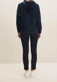 Navy blue hooded sweatshirt with a relaxed fit; paired with slim-fit navy denim; white sneakers. Simple design, no visible patterns or logos.