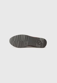 Semelle de chaussure en caoutchouc noir avec un motif texturé et strié ; présente un détail de marque circulaire et un emblème pour l'adhérence.