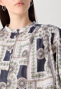 Blusa leggera con motivo a stampa e colletto alto, caratterizzata da disegni geometrici nelle tonalità blu notte, bianco e verde, con bottoni lungo il davanti.
