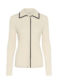 Kratka bežna pletiva s dolgimi rokavi, z gumbom spredaj, koničastim ovratnikom in črnimi valovitimi robovi vzdolž ovratnika in gumbne linije.