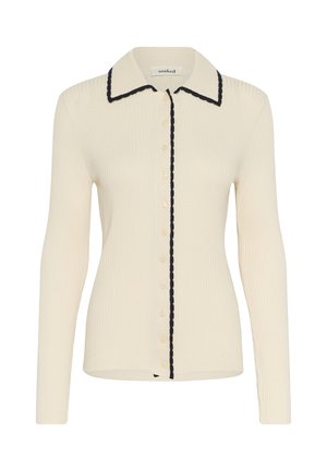 Langärmelige cremefarbene Rippenstrickjacke mit Knopfverschluss, spitzem Kragen und schwarzem gewelltem Rand entlang des Kragens und der Knopfleiste.