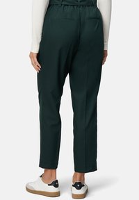 Groene, high-waisted broek gemaakt van zachte stof, met een relaxte pasvorm, zijzakken en een gladde textuur, gecombineerd met witte sneakers.