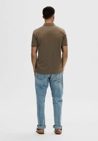 Brun kortärmad polo med krage, tillsammans med ljusblå avslappnade denimjeans och bruna sandaler, sedd bakifrån.