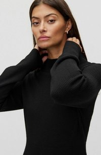 Sort ribbet sweater med høj krave, tætsiddende design og lange ærmer. Har tekstureret stof og sømløse skuldre.