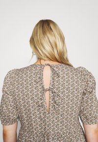 Kwiatowa sukienka z bufkami krótkimi rękawami, z zapięciem na wstążkę z tyłu oraz wzorzystą tkaniną w odcieniach różu, zieleni i kremu.