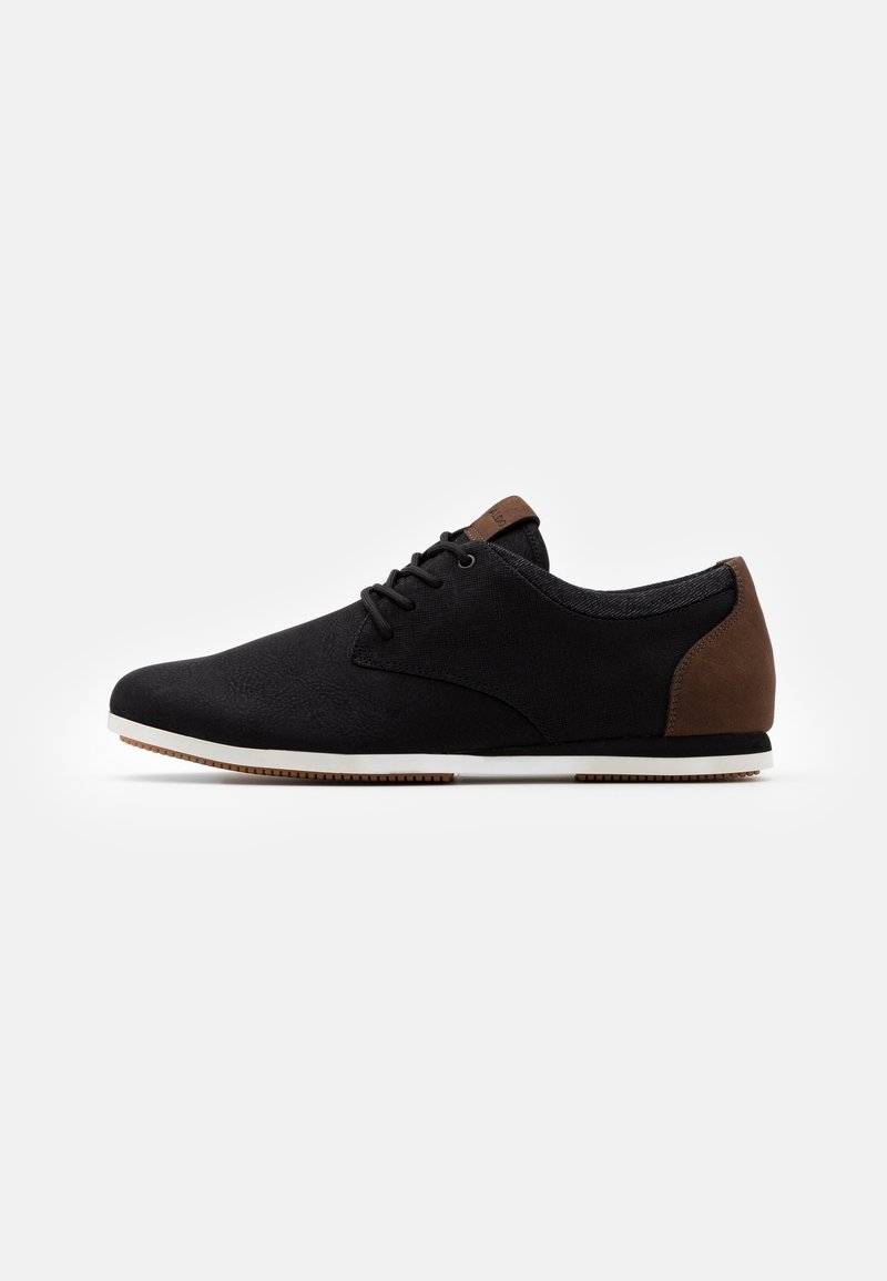 Basket décontractée noire avec un accent marron au talon, lacets noirs et semelle blanche, vue de profil sur fond blanc.