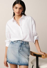 Witte button-up blouse met lange mouwen, gecombineerd met een lichtblauwe denim minirok met een rafelige zoom en frontzakken.