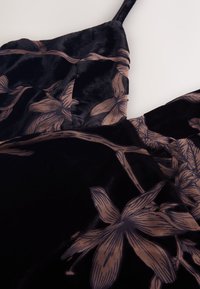 Abito in velluto nero con motivo floreale marrone, caratterizzato da spalline sottili e una texture morbida. Il design include foglie e fiori stampati su tutta la superficie.