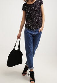 Černý top s krátkým rukávem a květinovým vzorem, modré džíny s vysokým pasem, černá kabelka a černé sandály na otevřené špičce.