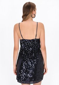 Elegáns tengerészkék flitteres miniruha vékony pántokkal, testhezálló felsőrésszel és bővülő szegéllyel, fényes textúrával és csillogó felülettel.