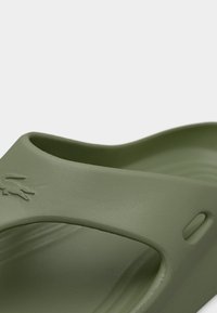 Grüne Slidesandale aus glattem, flexiblem Material. Verfügt über ein geschwungenes Design mit einem markanten Logo und einem strukturierten Fußbett für Komfort.