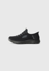 Black slip-on Skechers athletic shoe with mesh fabric, flexible sole, and pull tab on tongue, shown in left side profile on white background.