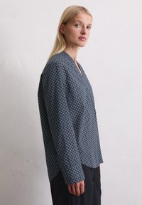 Navyblauw langermig shirt met V-hals, voorzien van een geometrisch wit patroon en een iets losse pasvorm, gemaakt van soepel materiaal.