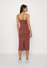 Vestido de comprimento médio, cor ferrugem, com alças finas, forma ligeiramente ajustada e uma fenda nas costas para facilitar os movimentos; confeccionado em um tecido suave.