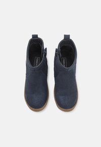 Botas de tornozelo azul marinho com um acabamento em camurça texturizada, fechos laterais com zíper e solas de borracha castanha. Design simples sem padrões visíveis.