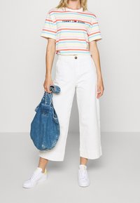 Gestreepte t-shirt in pasteltinten, witte wijde broek, blauwe denim tas en witte sneakers met gele accenten. Eenvoudig ontwerp en casual pasvorm.