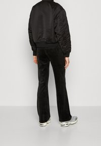 Veste bomber en satin noir avec ourlet froncé, associée à un pantalon noir évasé. La tenue est complétée par des chaussures de sport argentées.