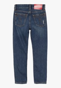 Tmavě modré denimové džíny se slim fit střihem. Obsahují dvě zadní kapsy s dekorativním švem. Kapsa na pasu s logem Calvin Klein Jeans.