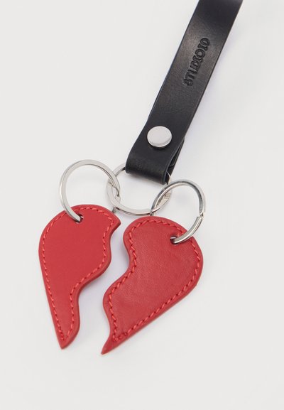 Μπρελόκ από κόκκινο δέρμα σε σχήμα δύο επικαλυπτόμενων ημίσεων καρδιάς, με μαύρο δερμάτινο λουράκι και ασημένιο μεταλλικό κρίκο για κλειδιά.