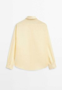 Chemise à manches longues en tissu jaune pâle doux, dotée d'un col classique, d'un ourlet arrondi et de poignets à boutons. Caractérisée par une texture lisse et légère.