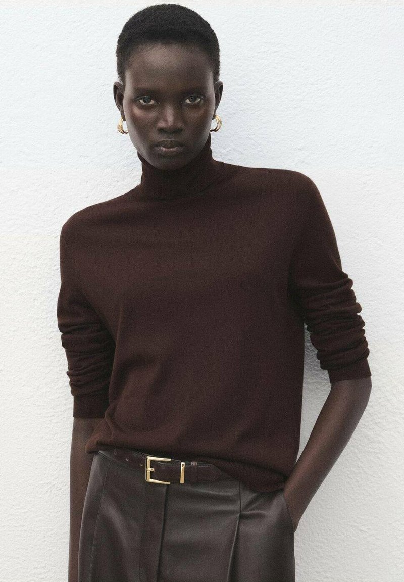 Pulover maro cu guler înalt, realizat din material moale, prevăzut cu mâneci lungi. Asociat cu pantaloni maro din piele cu talie înaltă și o curea cu accente aurii.