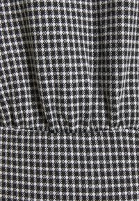 Mustavalkoinen houndstooth-kuvioinen kangas, jossa on teksturoitu pinta ja rypytetty yksityiskohta yläreunassa.