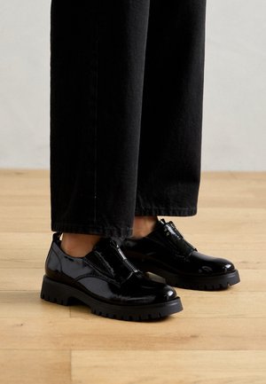 Læder sko i sort patentlæder med en kraftig sål og lynlås. Glat tekstur med et strømlinet design, synlige syninger og hævet hæl.