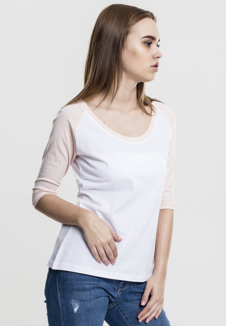 T-shirt con maniche raglan in cotone bianco con maniche rosa chiaro. Presenta un collo a giro morbido e una vestibilità comoda, abbinato a jeans di denim.