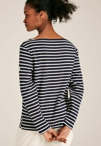 Námornícky a biele pruhované tričko s dlhým rukávom a širokým výstrihom, s bočným rozšírením a malou logom nášivkou na ľavom rukáve.