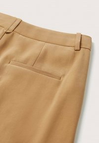 Pantalon beige sur mesure avec une poche passepoilée à l'arrière, des passants de ceinture et une couture au centre de la taille arrière.