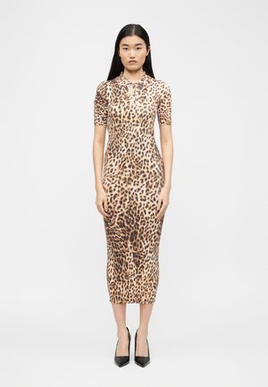 Femeie în picioare purtând o rochie midi mulată cu imprimeu leopard, mâneci scurte și nasturi la guler, asortată cu pantofi negri cu vârf ascuțit.