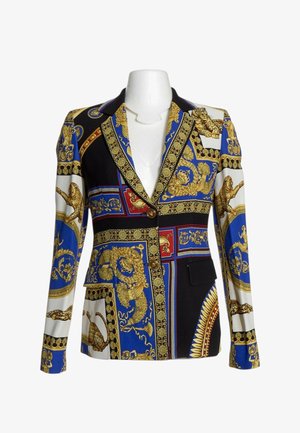 Blazer con patrones barrocos dorados, paneles azules, negros, rojos y blancos, motivos de leopardo y botones decorativos sobre un maniquí blanco.