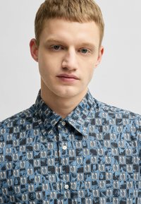 Overhemd met knoopsluiting in een blauw patroon met bladvormen, gestructureerde kraag en een gladde stoftextuur.