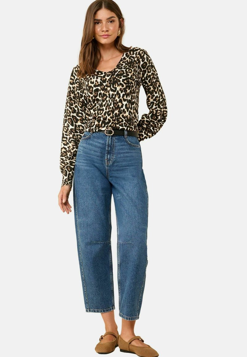 Top de manga larga con estampado de leopardo combinado con jeans azul de tiro alto. Los jeans tienen piernas rectas y dobladillos enrollados. Unos zapatos marrones de tipo slip-on completan el look.