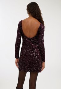 Abito senza maniche, scoperto sulla schiena, di un profondo color bordeaux con texture di paillettes, forma aderente e leggera elasticità, che arriva a metà coscia.