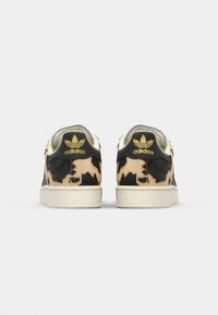 Baskets avec un upper à imprimé léopard beige et noir, dotées d'une languette de talon noire et d'un logo Adidas doré, ainsi qu'une semelle en caoutchouc couleur crème.