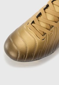 Gullfarget fotballsko med teksturert læroverdel, fremtredende sømmer, flate lisser og en avrundet tå for et strømlinjeformet design.