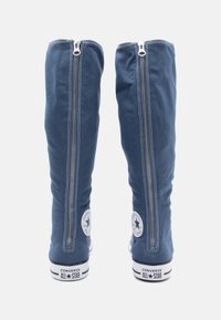 Blaue Canvas-Stiefel in hoher Form mit silbernen Reißverschlussdetails und runden Markenpatches. Gummisohlen mit schwarz-weißen Streifenakzenten an der Unterseite.